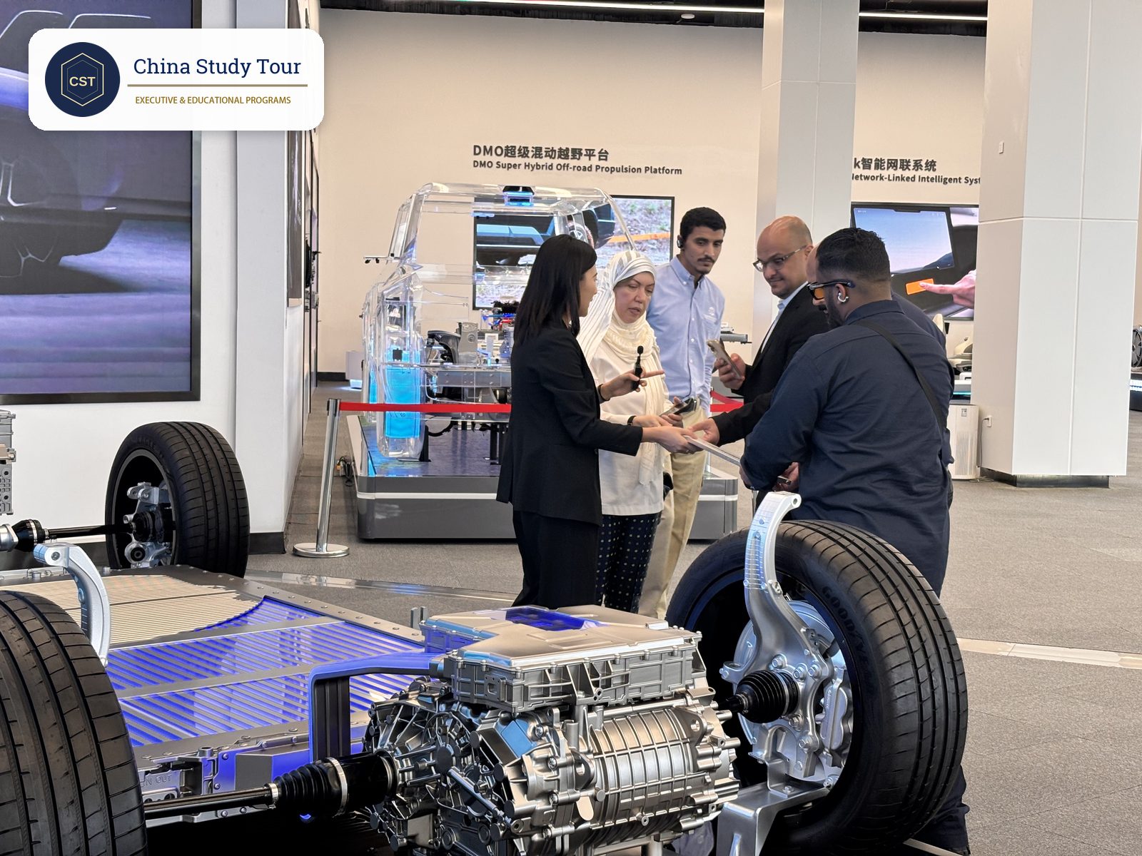 BYD guide explaining an electric vehicle chassis to the Saudi delegation in front of the DMO Super Hybrid Off-road Platform