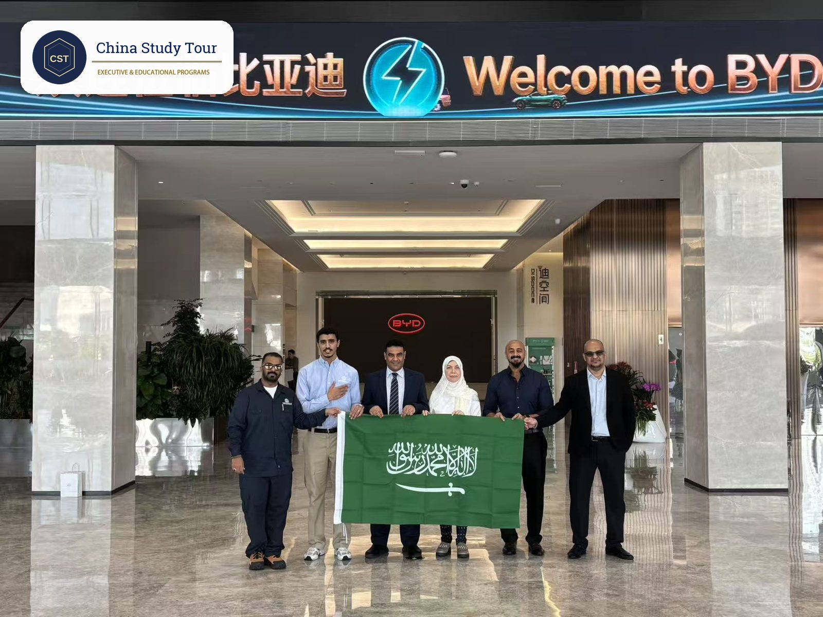 Saudi delegation holding their national flag under the Welcome to BYD screen at the start of a BYD headquarters tour in Shenzhen